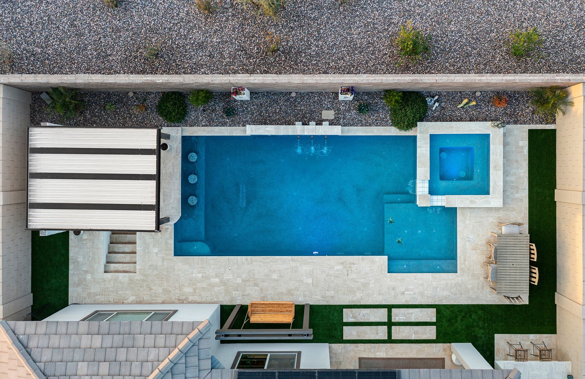 Overhead view of a rectangular backyard pool with a hot tub, shaded seating area, and artificial grass.