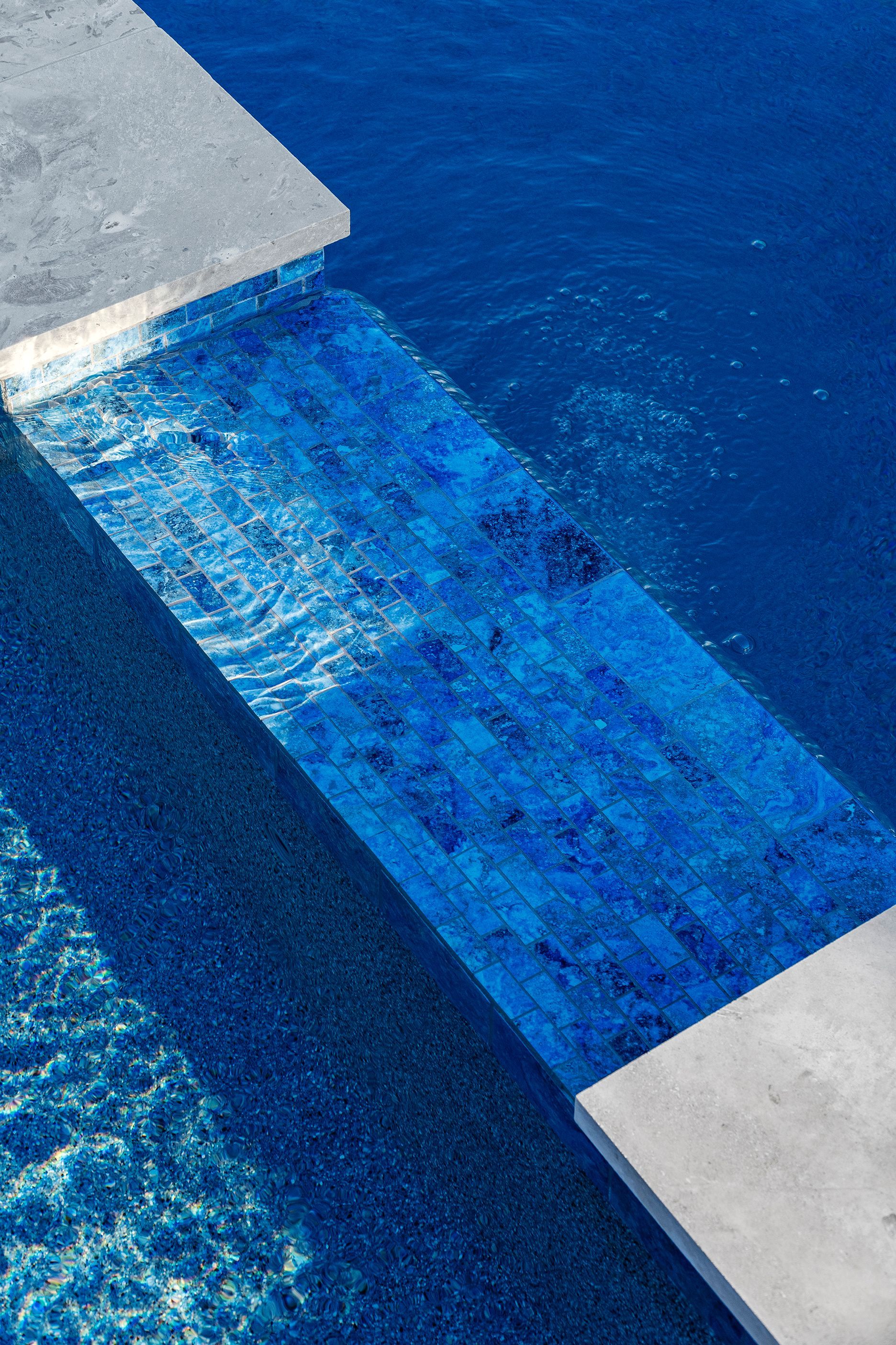 Blue tiled steps descend into a pool of deep blue water, with concrete edging.