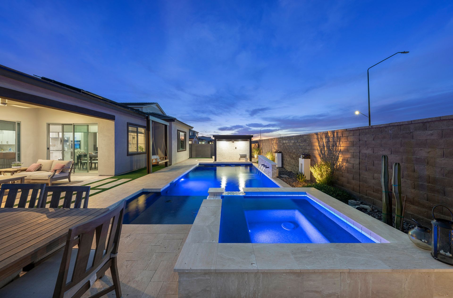 Backyard pool at dusk with illuminated water; modern home and patio.