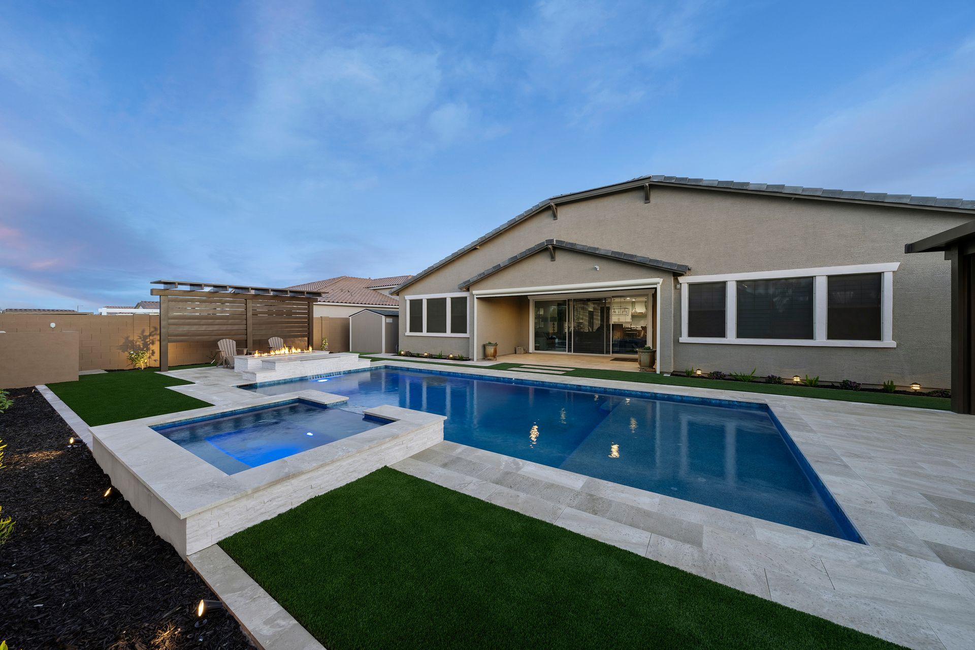 Backyard with a pool and spa next to a house under a blue and cloudy sky.