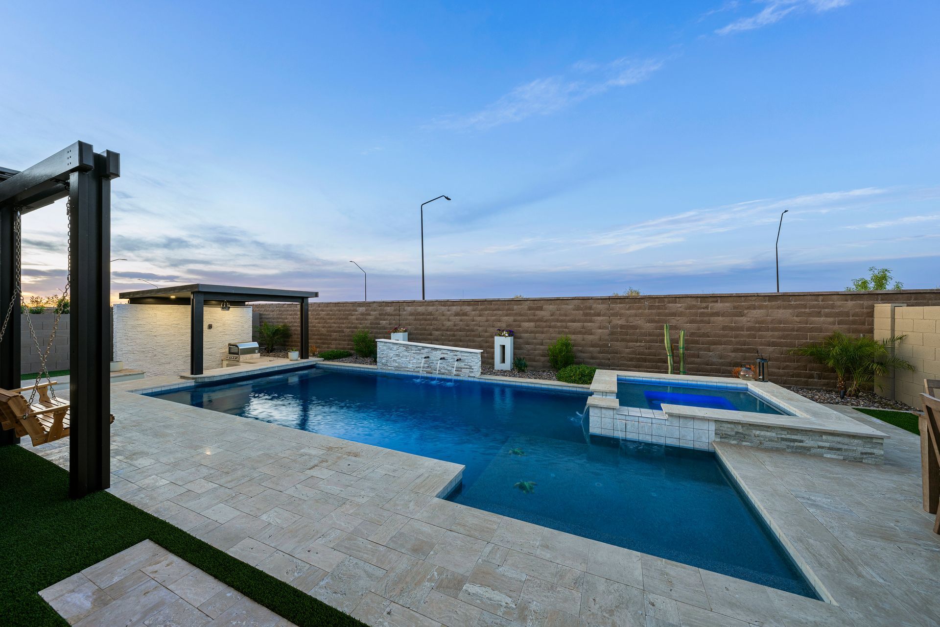 Backyard pool with spa, landscaping, and pergola under a blue sky.