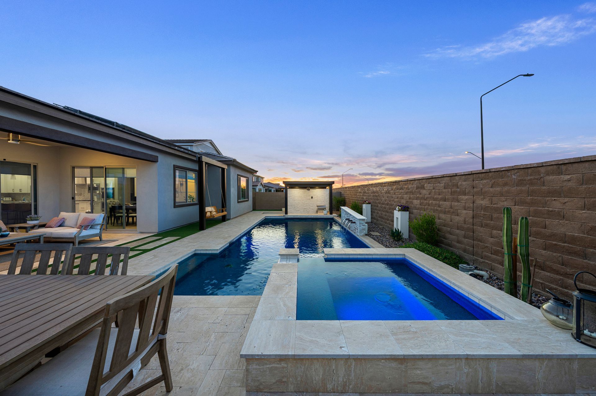 Backyard with pool and spa, patio furniture, and a building under a blue sky.