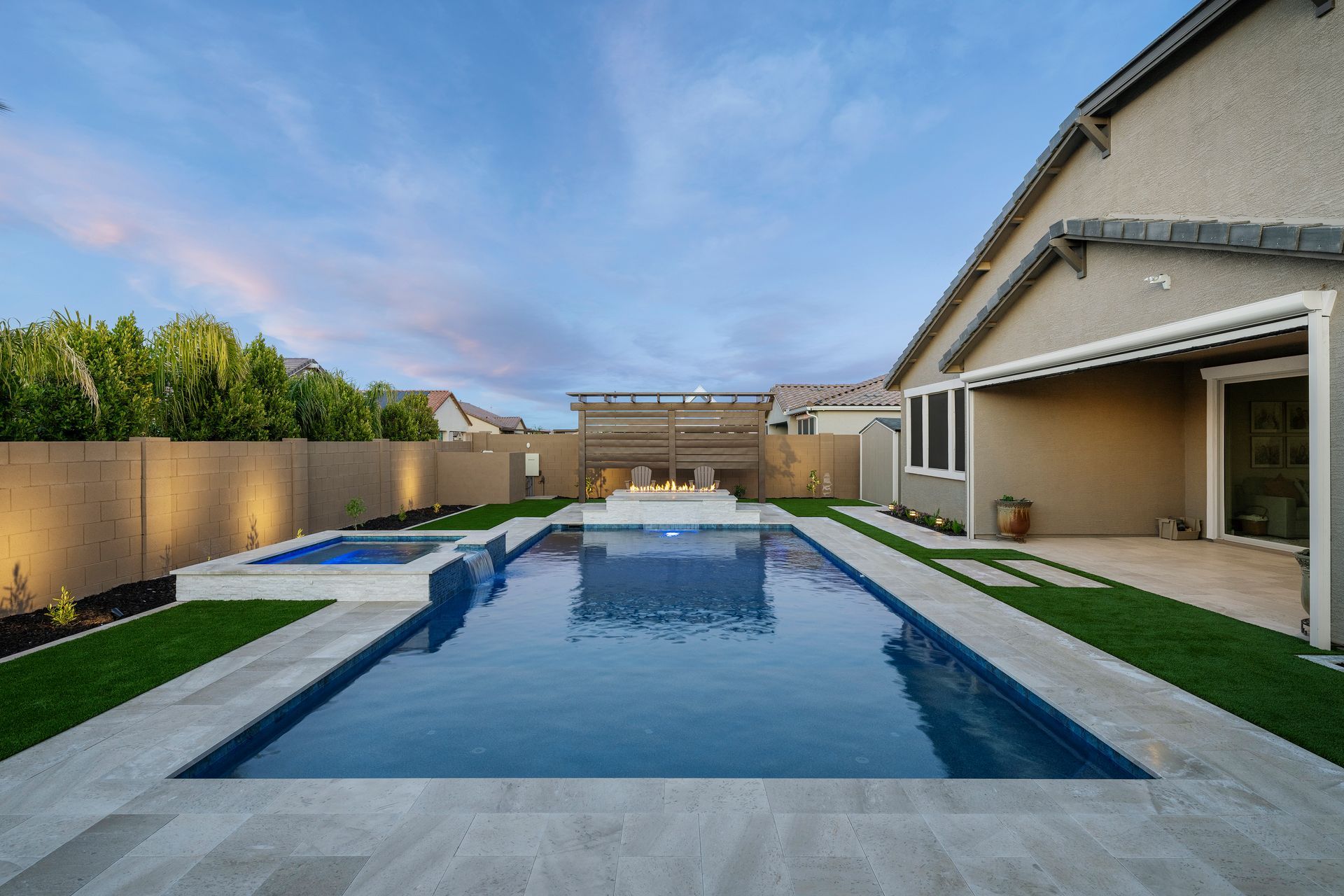Backyard pool with spa, lawn, and house under a twilight sky.