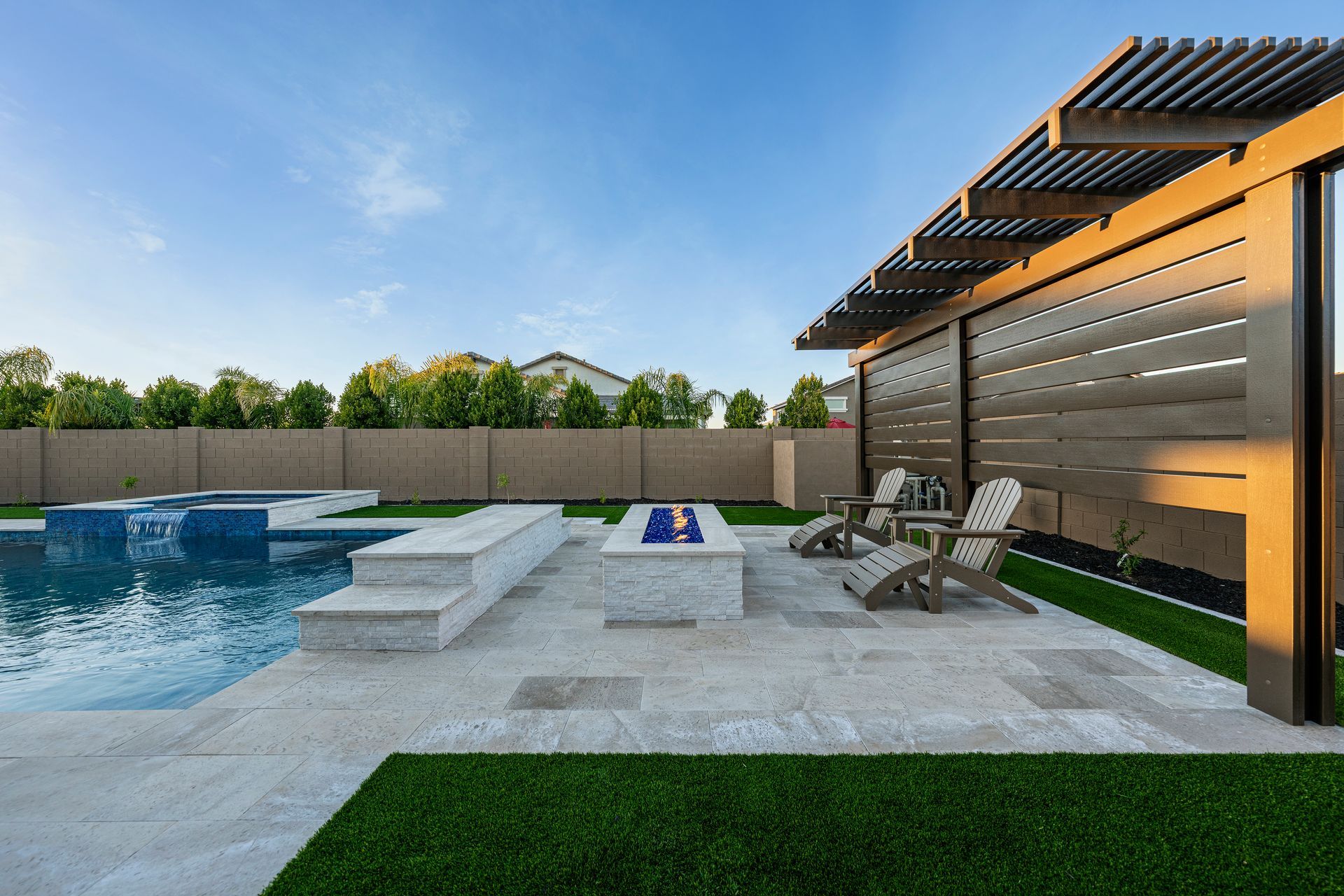 Poolside patio with fire pit, seating, and pergola under a blue sky.