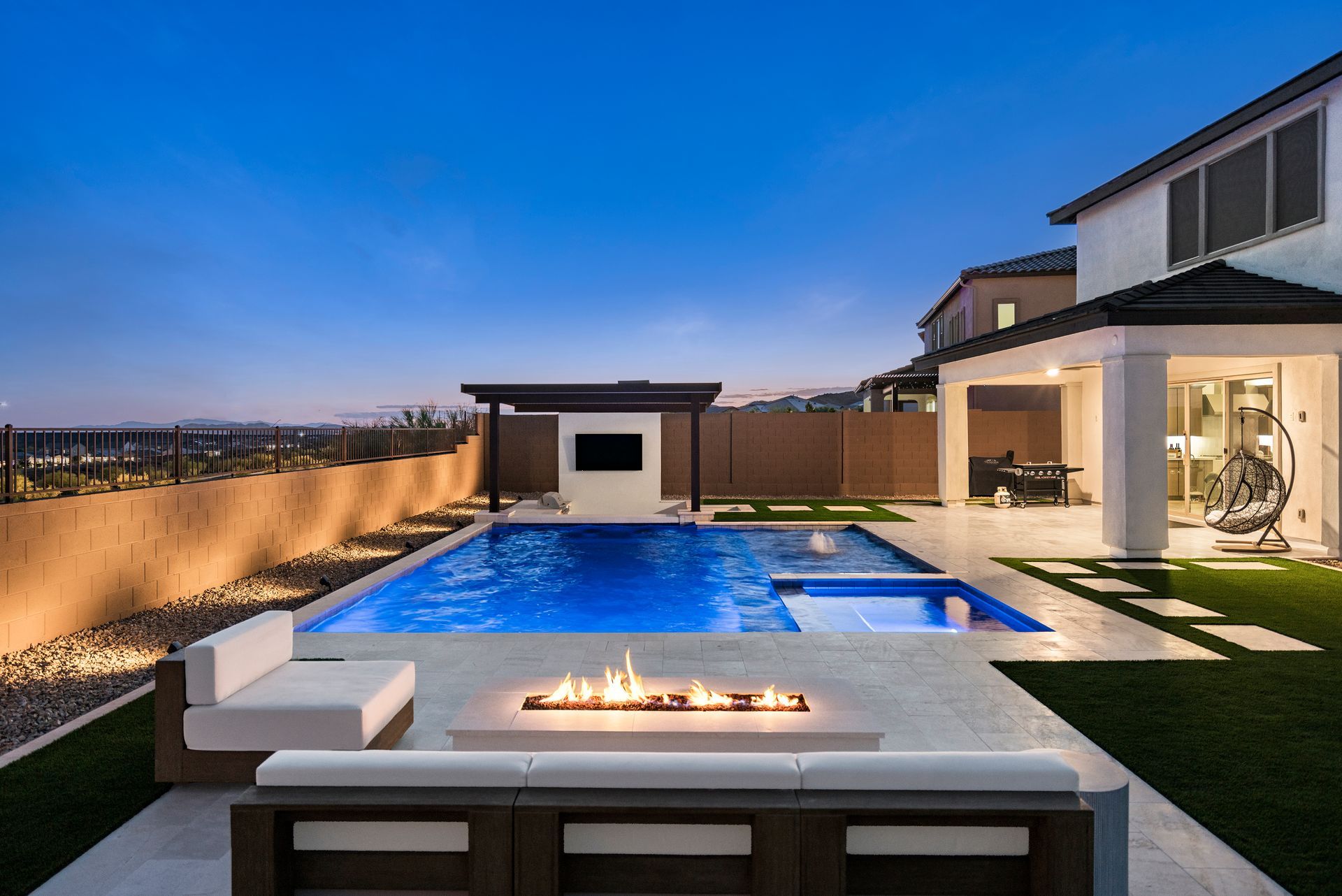Backyard with pool, outdoor fireplace, seating area, and modern home at dusk.