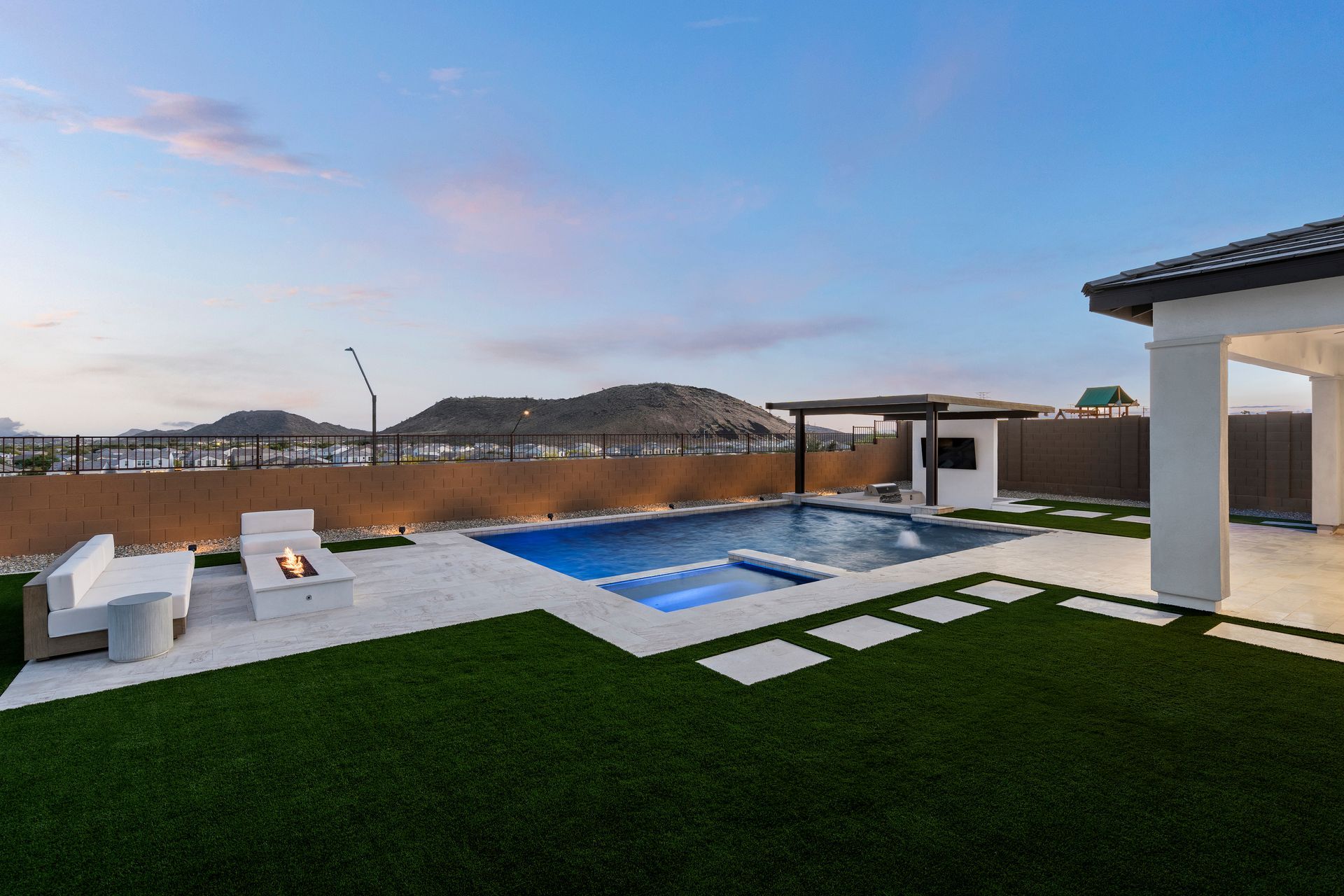 Backyard with a pool and fire pit, green lawn, mountains in the distance, and a partially visible house.
