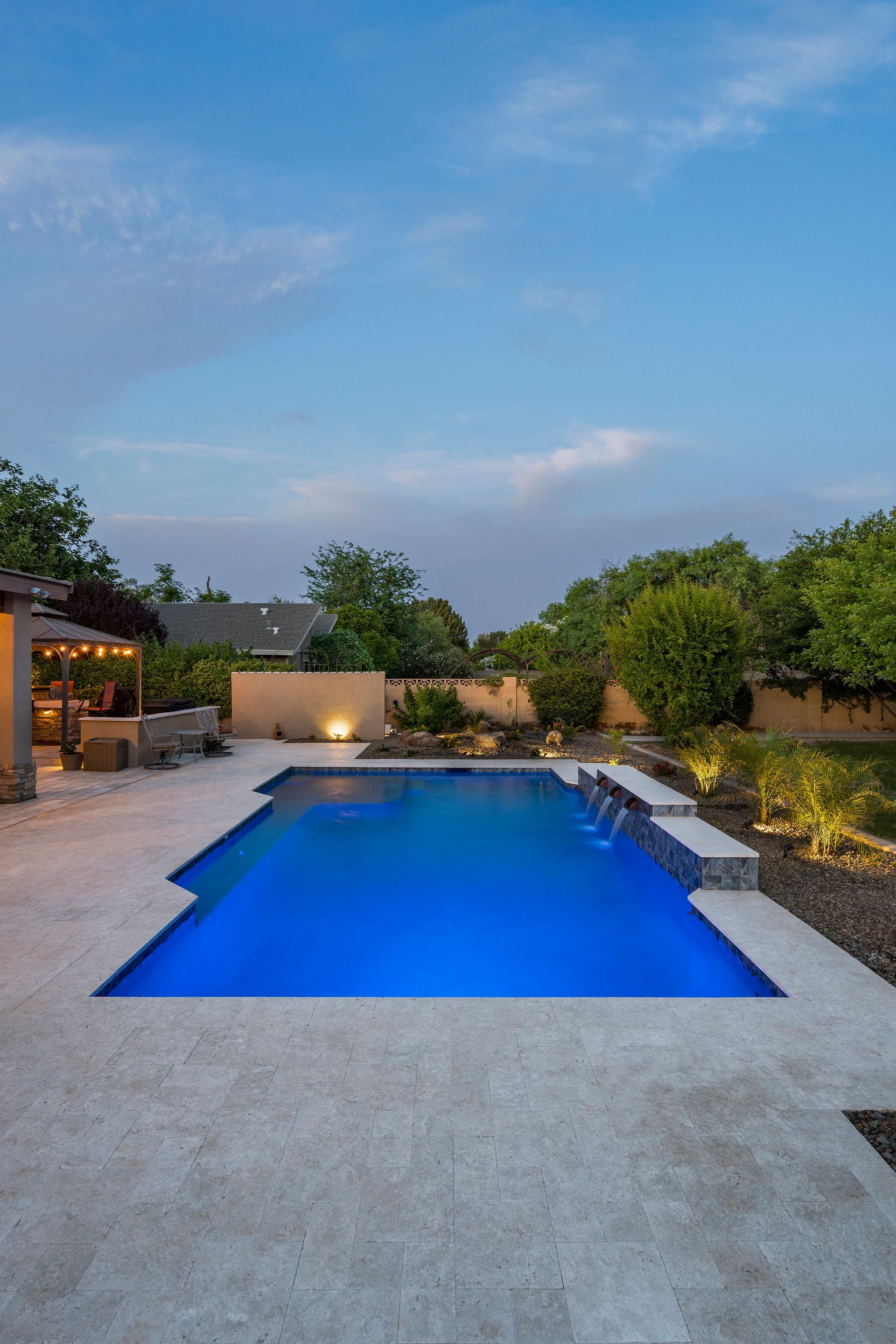 Backyard pool with blue water and stone patio under a dusky sky.