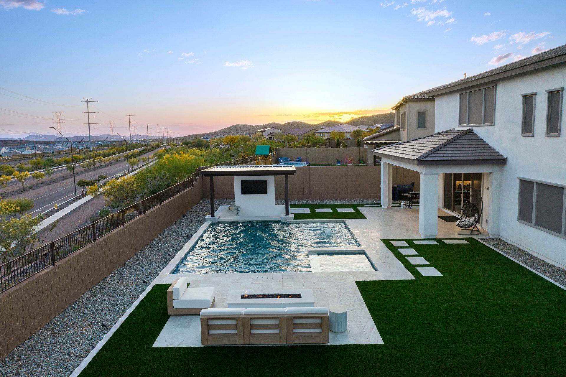 Backyard with a pool, patio, and outdoor seating. House in the background. Sunset over the hills.