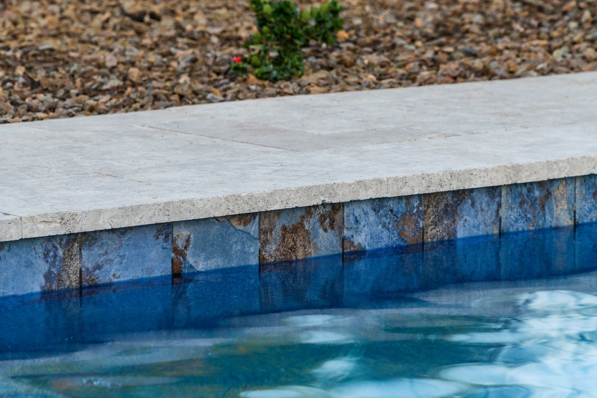 Pool coping and tile edge at the water line, with a stone border and tan coping.