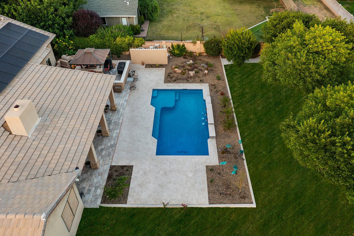 Aerial view of a backyard with a blue rectangular pool, patio, and green lawn.