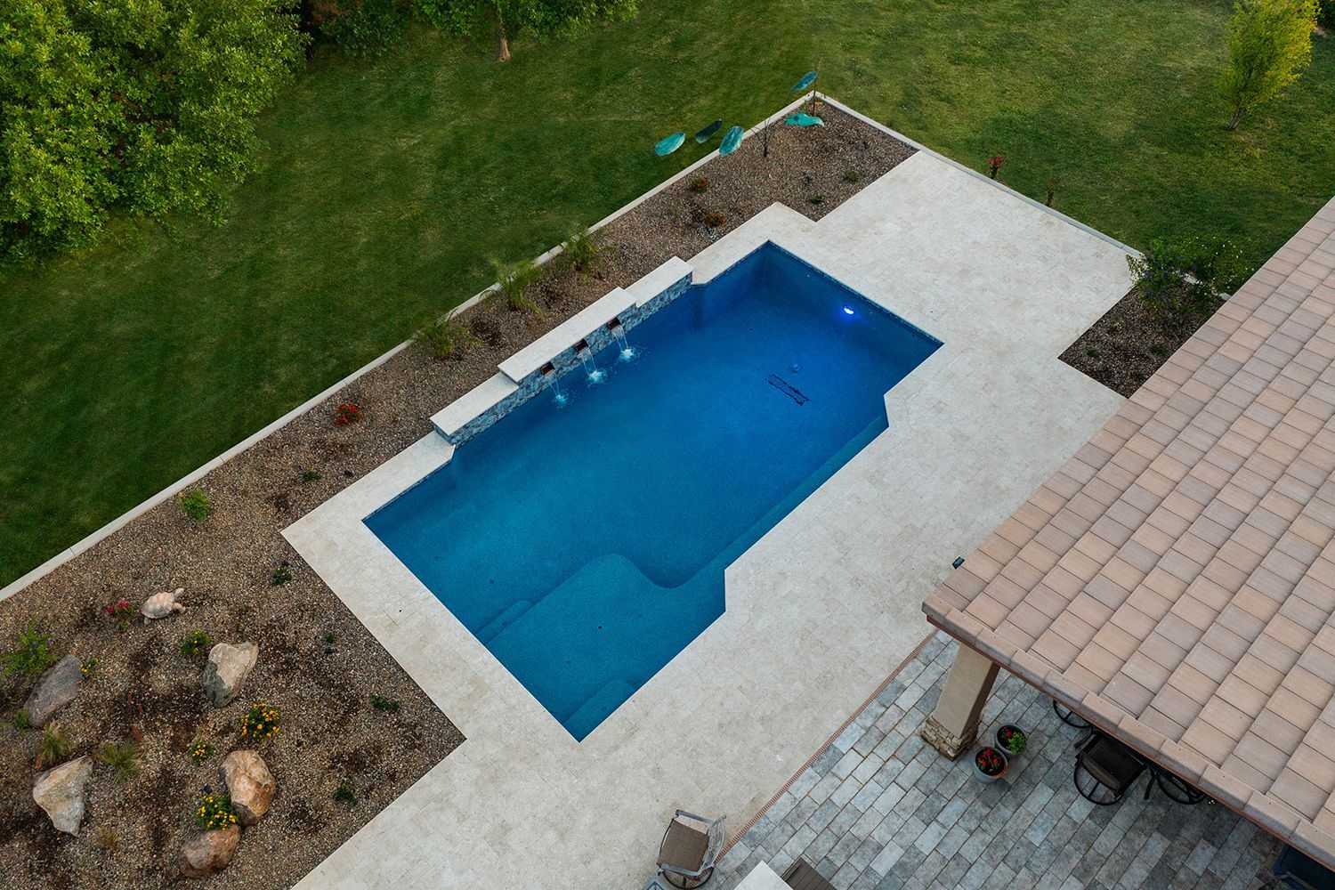 Aerial view of a rectangular blue pool with a waterfall feature surrounded by light concrete and green lawn.