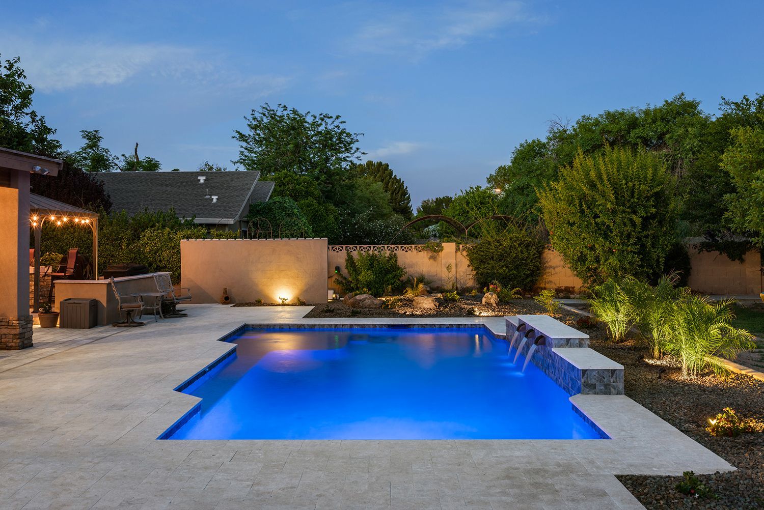 Pool at dusk with blue water, patio, and illuminated landscaping.