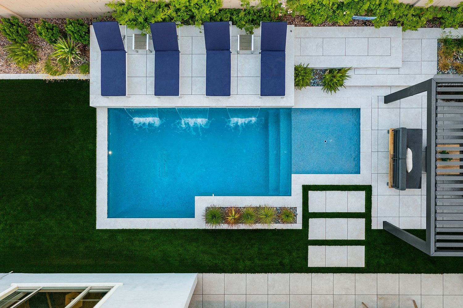 Overhead view of modern backyard with blue pool, lounge chairs, and artificial turf.