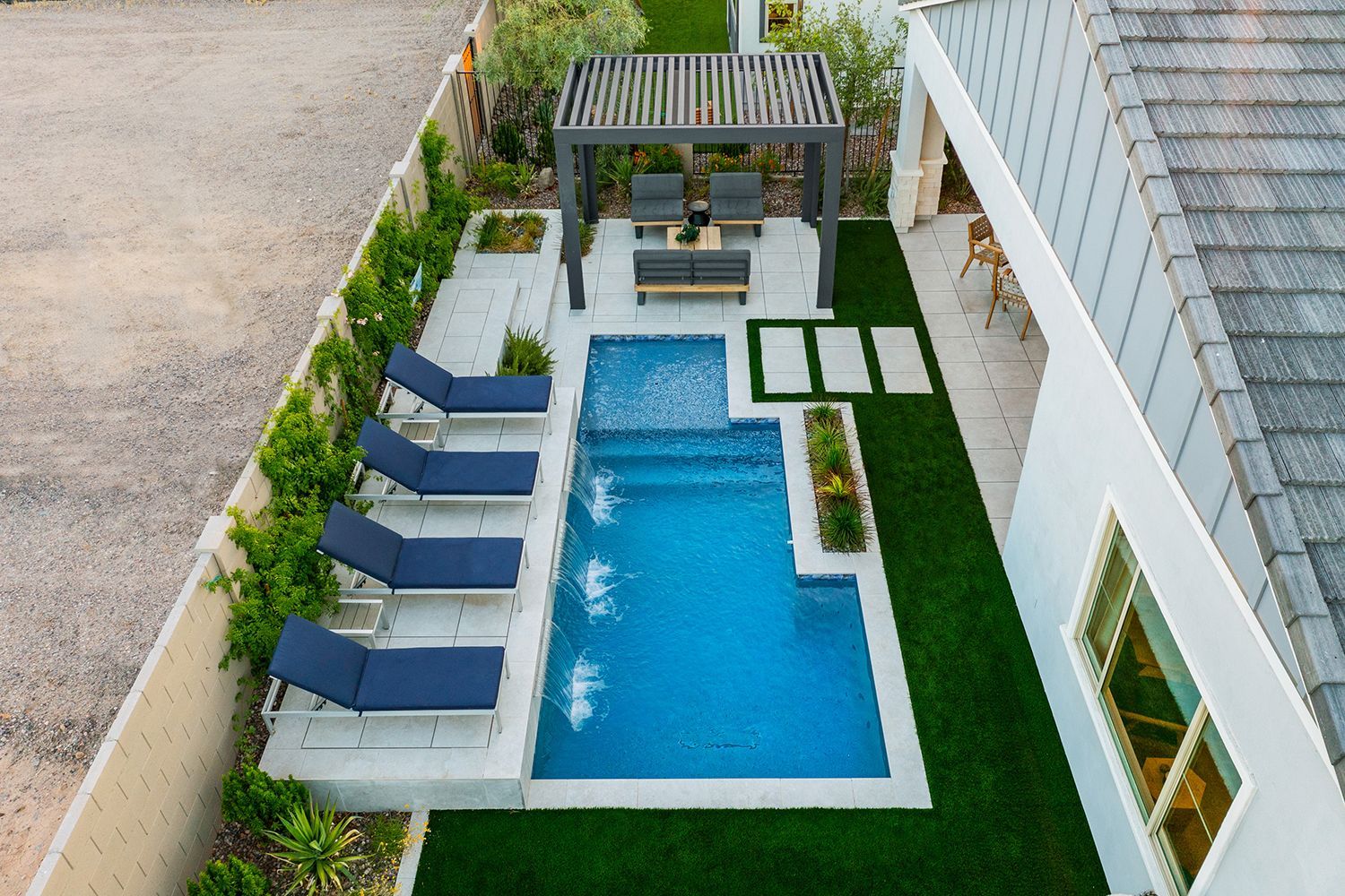 Aerial view of a backyard with a pool, lounge chairs, pergola seating area, and artificial grass.