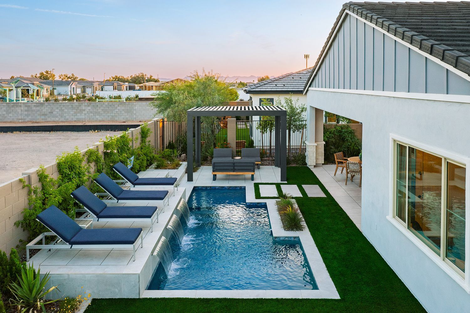 Backyard pool with lounge chairs, pergola, and house exterior. Blue pool, green grass, and gray accents.