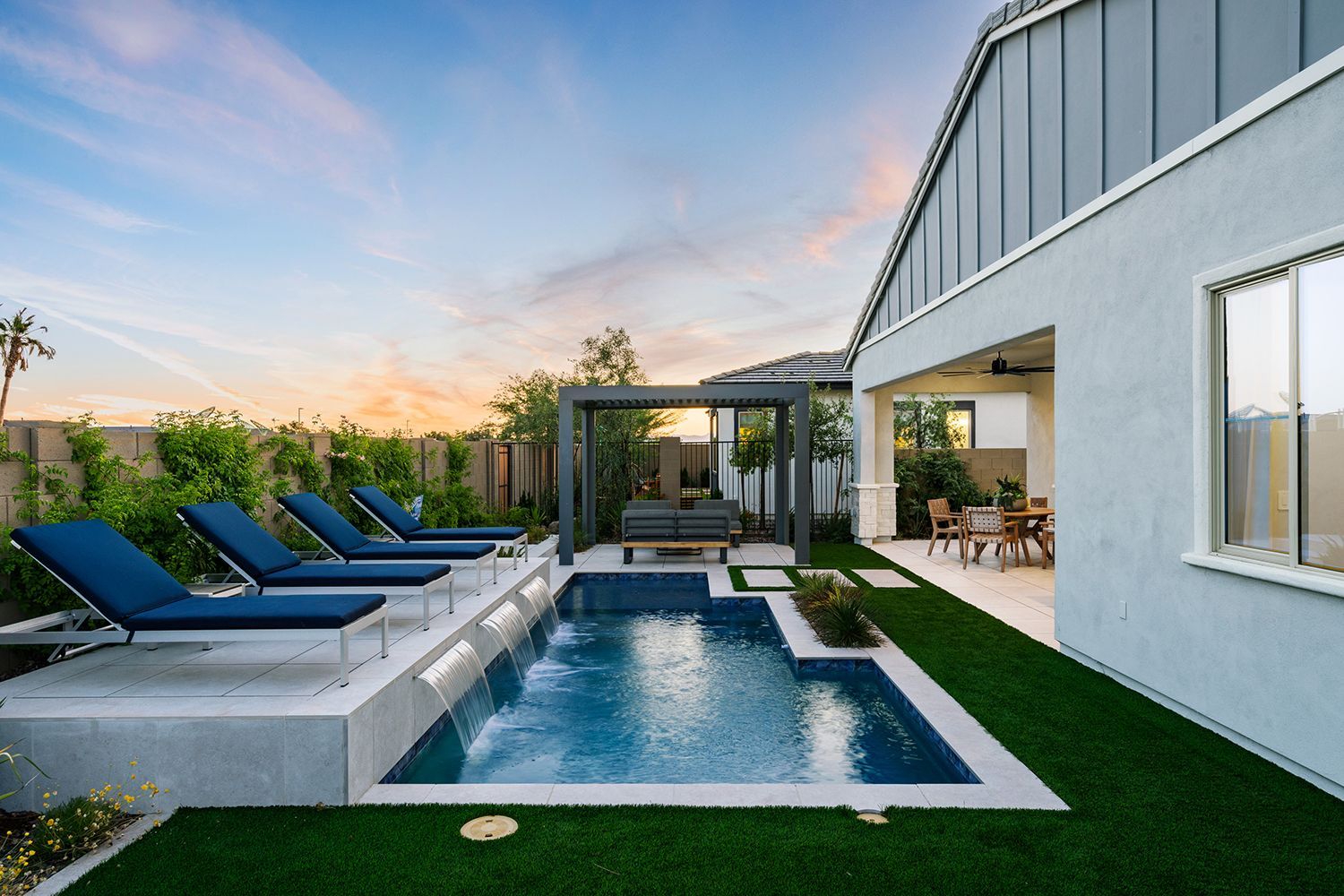 Pool area with blue lounge chairs, pool, and house exterior; sunset sky.