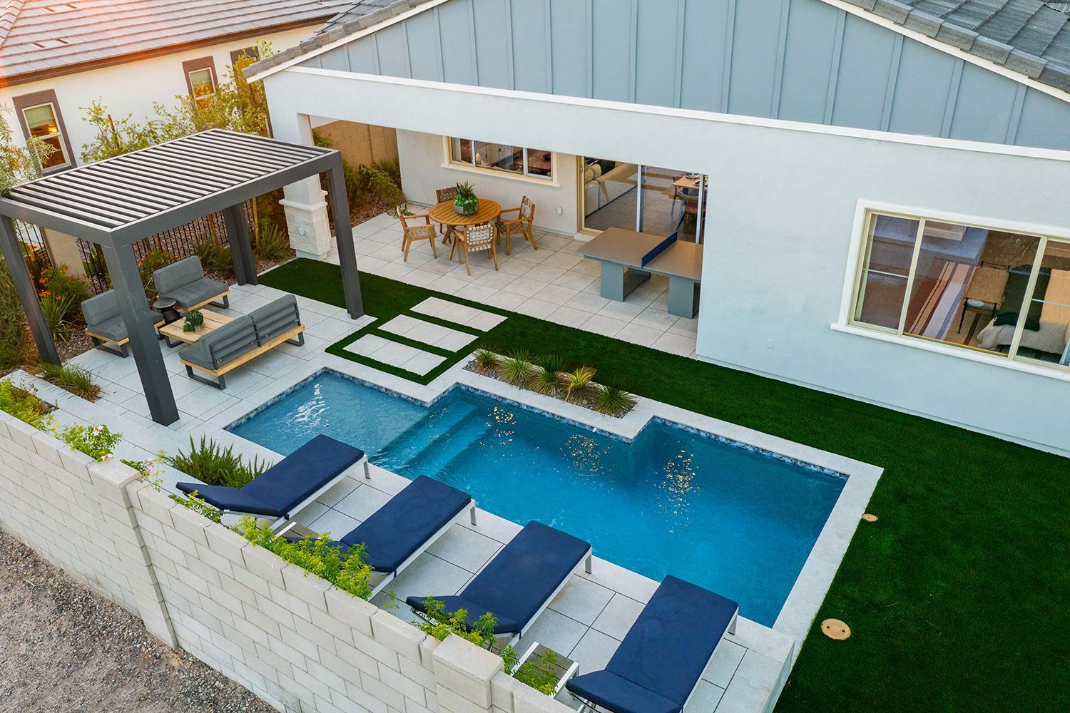 Modern backyard with pool, patio, and pergola; gray and blue tones with artificial grass.