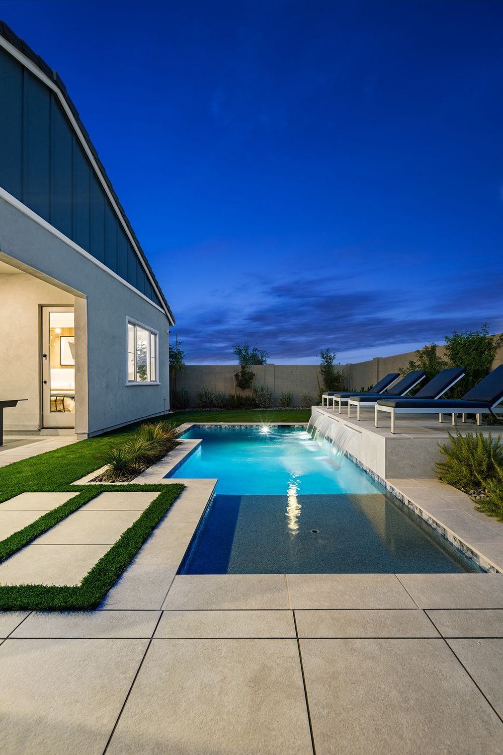Backyard pool at dusk; turquoise water, modern patio, lounge chairs, blue house.