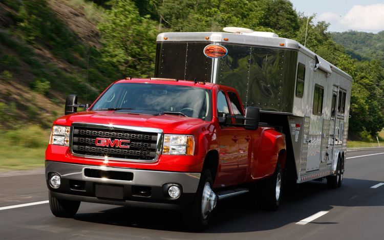 A red truck is towing a trailer on a highway.