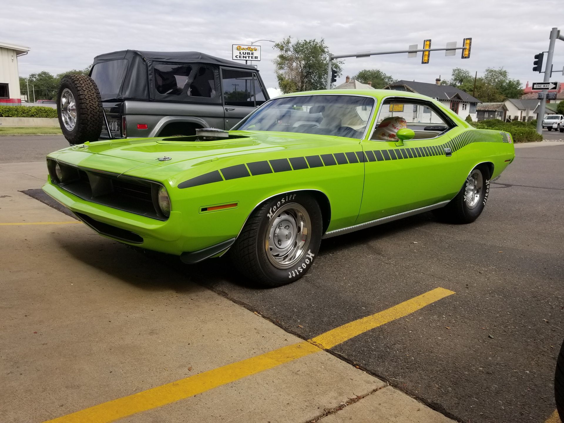 A green car is parked in a parking lot next to a jeep.