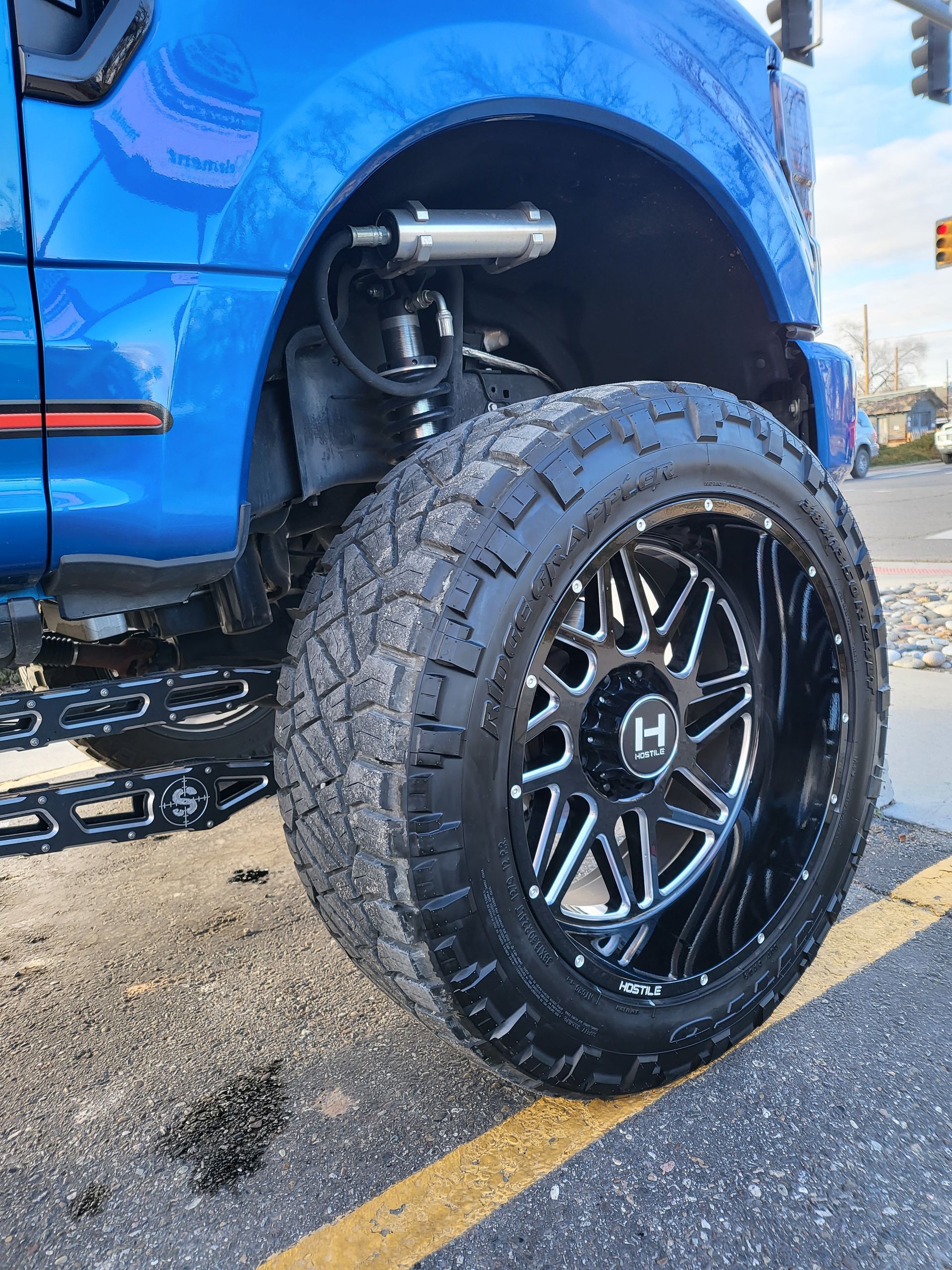 A blue truck with black wheels and tires is parked in a parking lot.
