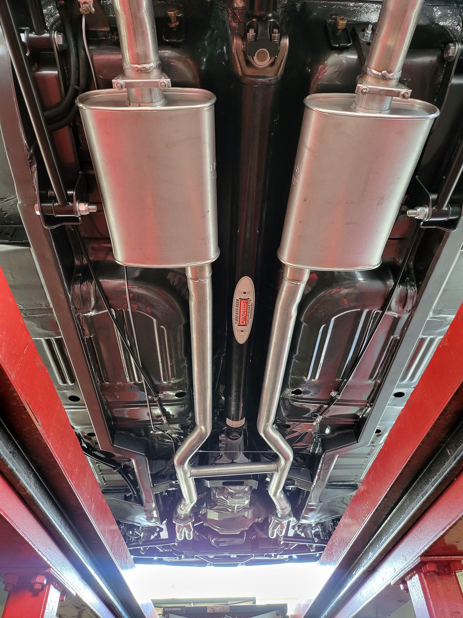 The exhaust pipes of a car are visible underneath it in a garage.