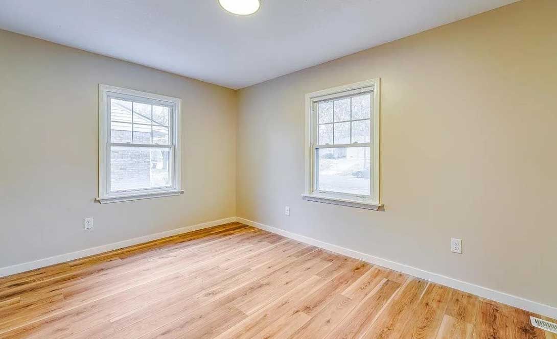 An empty room with hardwood floors and two windows.