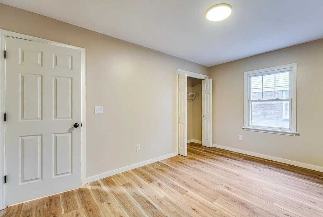 An empty bedroom with hardwood floors and a window.