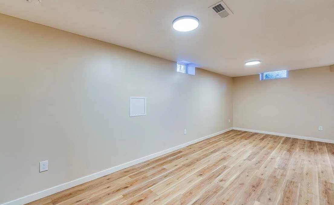 An empty basement with hardwood floors and white walls.
