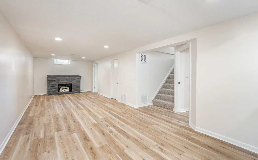 An empty basement with hardwood floors and a fireplace.