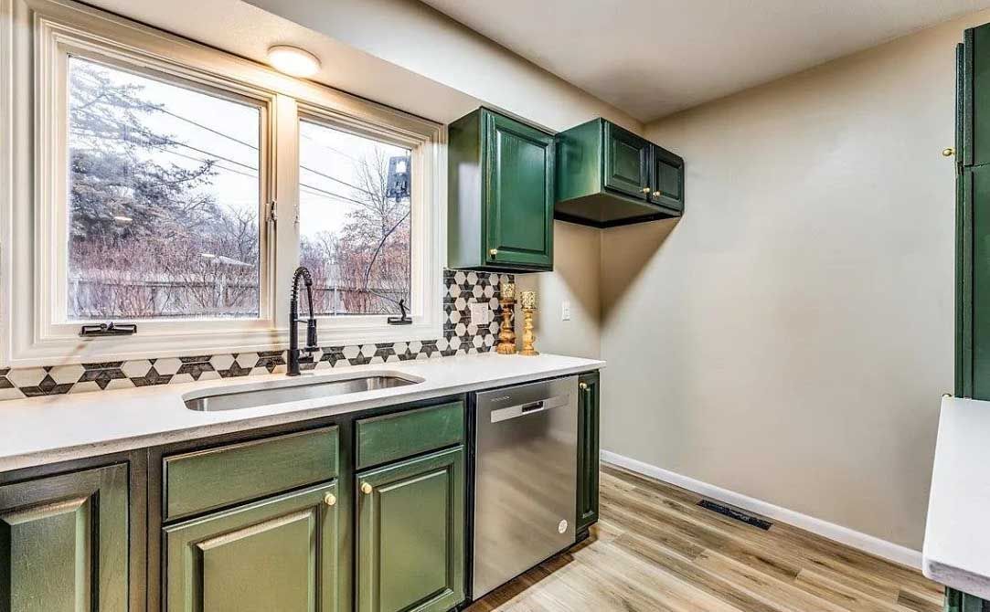 A kitchen with green cabinets , stainless steel appliances , a sink , and a window.
