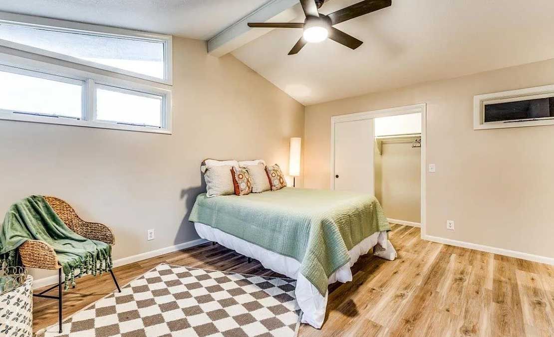 A bedroom with a bed , chair , rug and ceiling fan.