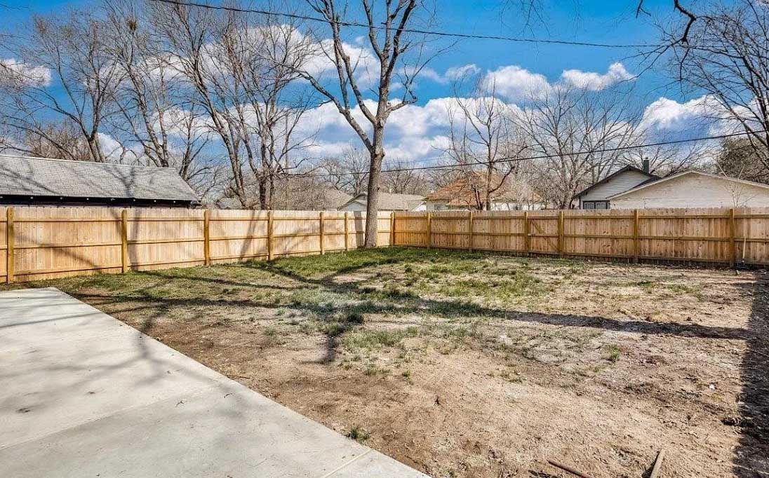 A backyard with a wooden fence and a concrete driveway.