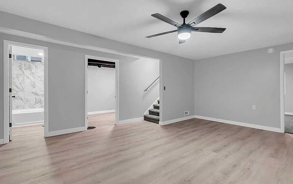 An empty basement with hardwood floors and a ceiling fan.