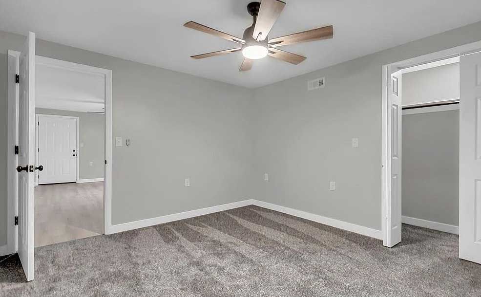 An empty bedroom with a ceiling fan and a closet.