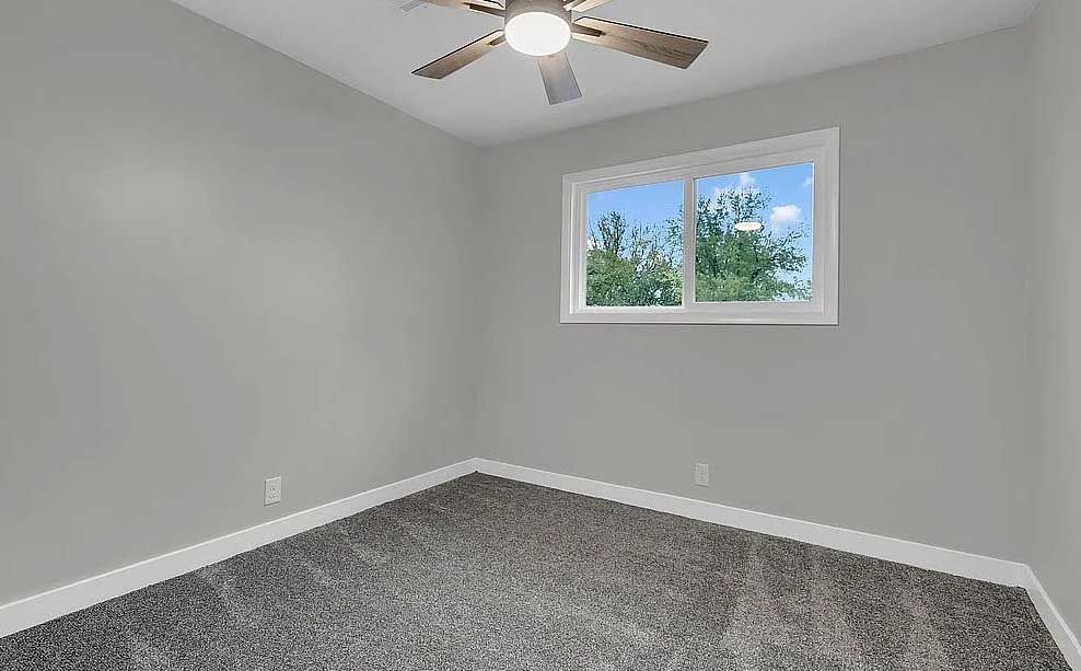An empty bedroom with a ceiling fan and a window.