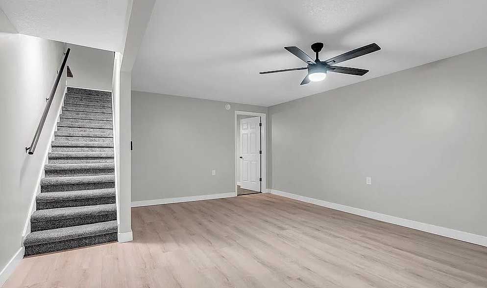 An empty living room with hardwood floors and stairs and a ceiling fan.