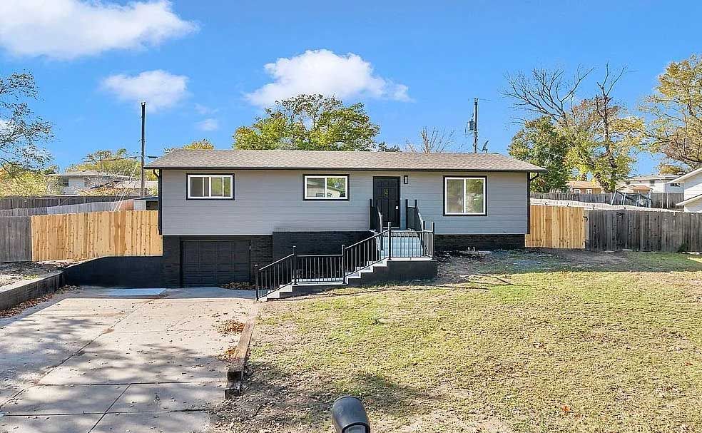 A gray house with a wooden fence and stairs is for sale.
