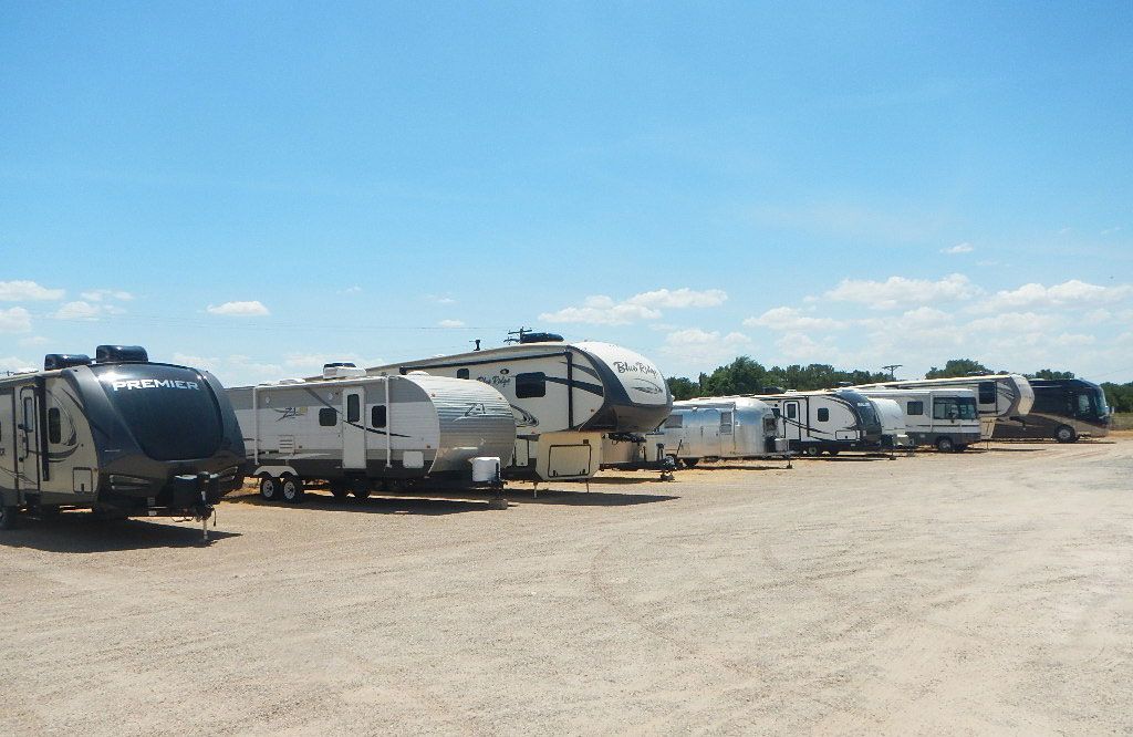 A row of recreational vehicles are parked in a gravel lot.