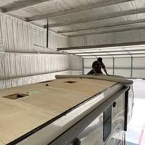 A man is working on the roof of a rv in a garage.