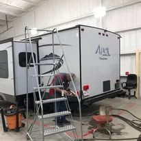 A man is standing on a ladder next to a trailer in a garage.