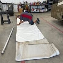 A man is kneeling on a piece of white fabric in a garage.