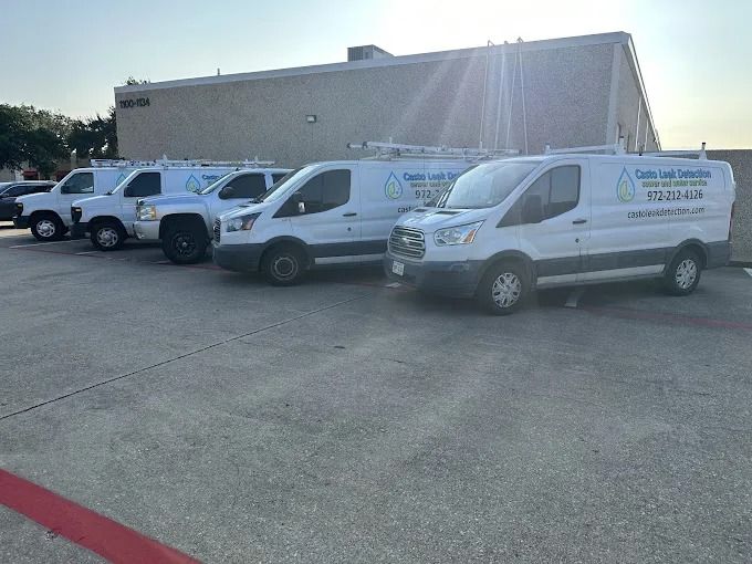 Four white service vans parked in a row in a concrete lot in front of a tan commercial building.