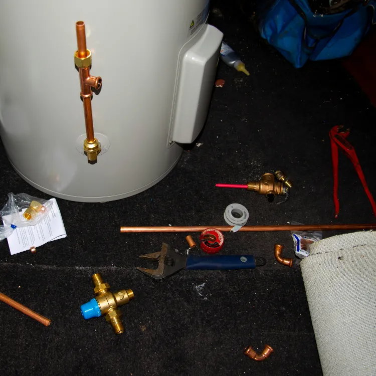 A partially installed water heater with copper pipes, brass fittings, and plumbing tools scattered on a dark surface.