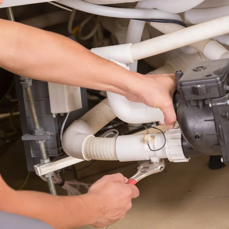 A person uses a wrench to tighten a fitting on white PVC plumbing pipes connected to a black pump motor.