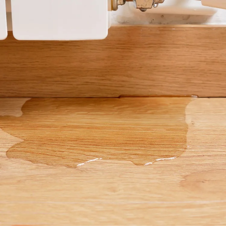 Water pooling on a wood floor beneath a radiator valve, indicating a leak.