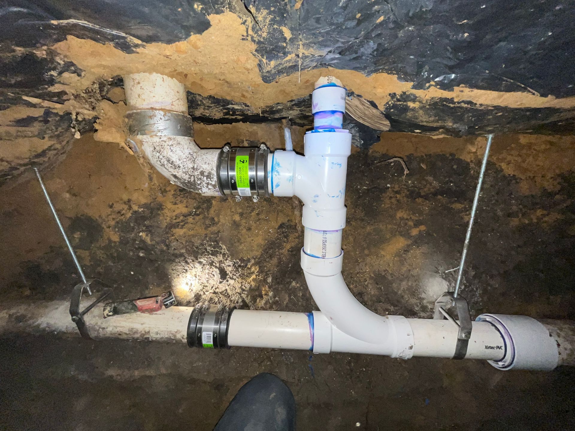 Exposed under-sink drain pipes and fittings in a wall cavity, with white PVC and a green coupling.