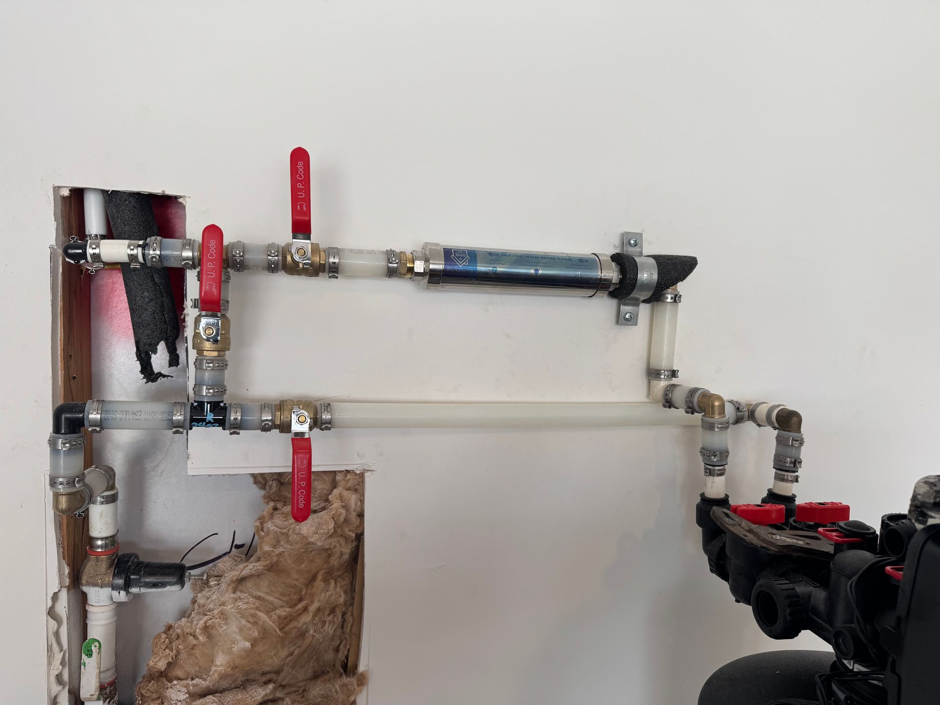 Plumbing pipes with red valves connected to a black pump on a wall.