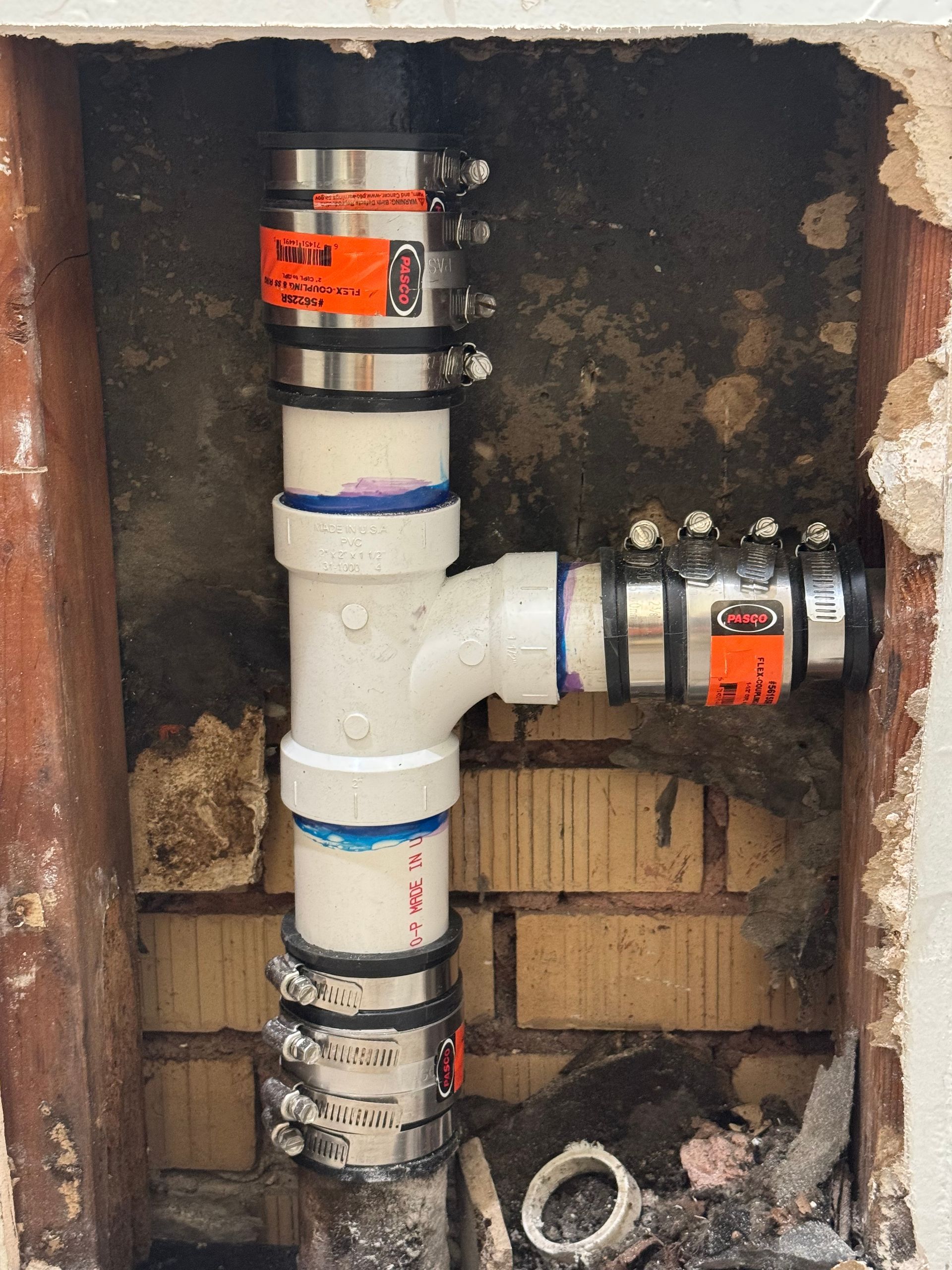 Plumbing pipes and couplings inside a wall opening, with an exposed vertical white pipe and a horizontal connection.