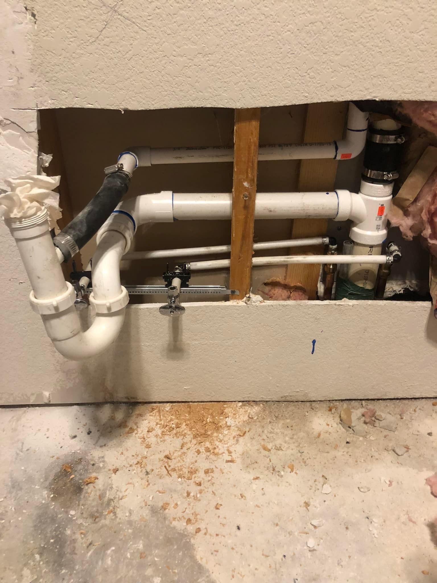 A wall cutout revealing white PVC plumbing pipes, including a P-trap, connected to a vertical drain line in a room.